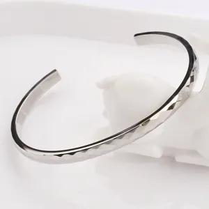 Bracelet jonc ouvert pour homme en métal argenté avec design de surface taillé à facettes.