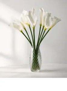 Vue de détail rapprochée de lis calla artificiels blancs dans un vase en verre transparent.