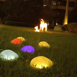 Gedetailleerd nachtzicht van kleurrijke solar LED stenen lampen op het gras in de tuin.