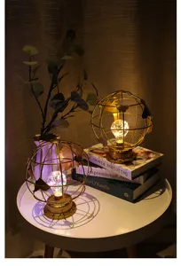 Close-up van gouden ijzeren globe nachtlamp met warme LED-lamp op witte tafel met boeken.