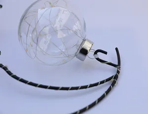 Detail view of transparent glass ball ornament with inner LED string lights and bracket.