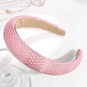 Dettaglio fascia imbottita con perline rosa, elegante accessorio per capelli intrecciato.