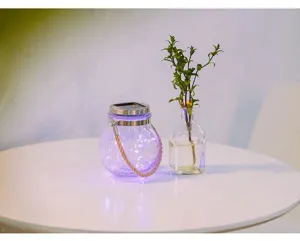 Detailed view of solar crackle glass hanging jar light emitting purple glow on a white table.