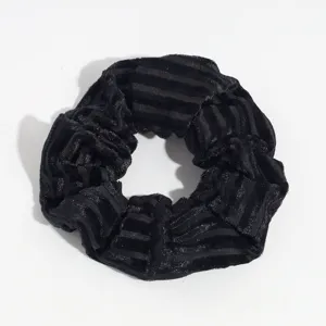 Detailed close-up of a black velvet hair scrunchie showing soft striped fabric texture.