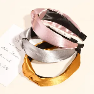 Nahaufnahme von drei satinierten Haarreifen mit Knoten in Rosa, Silber und Gold, fein.