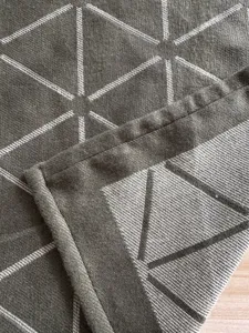 Detailed close-up view of a dark grey woven jacquard blanket with white geometric patterns.