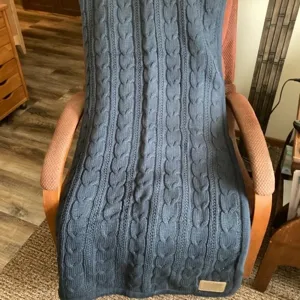 Detailed shot of a thick cable knit blanket draped over a cozy wooden armchair indoors.
