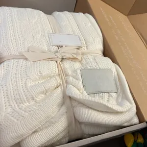 Cozy white cable knit throw blanket with ribbon tie in gift box, warm winter home decor.
