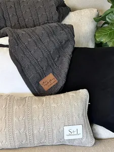 Detail view of cozy cable knit blanket and cushion with decorative patch on sofa.