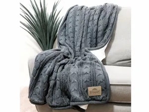 Close-up detail of the dark grey knitted cable blanket draped on a cozy sofa showing texture.