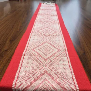 Chemin de table tissé rouge et blanc avec motifs géométriques et pompons pour décoration.