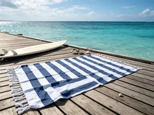 Scena di telo mare a righe blu e bianche su molo in legno vicino al mare con frange e surf.