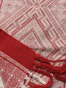 Détail en gros plan du chemin de table géométrique tissé rouge et blanc à franges.