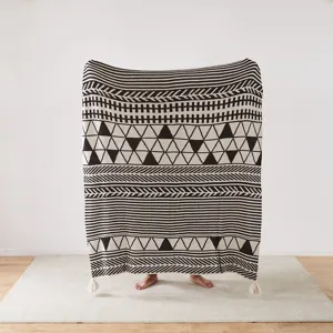 Black and white geometric knitted throw blanket with tassels for cozy home decor styling.