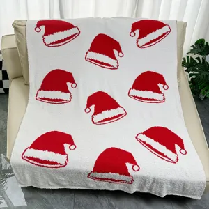 Couverture de Noël blanche et duveteuse avec un motif festif de chapeau de Père Noël rouge.