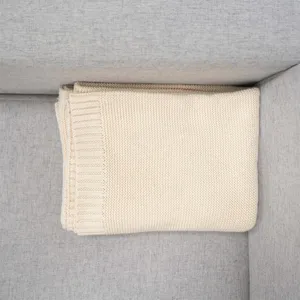 Close-up detail of cozy knitted blanket texture, soft ribbed edge design on gray sofa.
