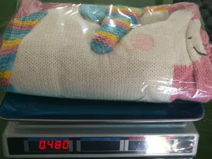 Detailansicht der handgestrickten Einhorndecke in transparenter Verpackung auf Waage.