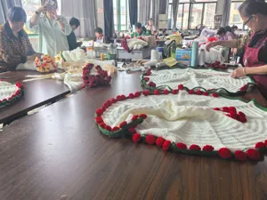 Handmade white crochet blanket with red floral pom-poms and green decorative edge.