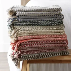 Gros plan detaille de couvertures jacquard tissees a franges empilees sur un tabouret.