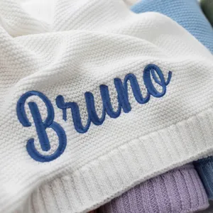 Close-up of white knitted blanket with custom blue Bruno embroidery, soft detail.