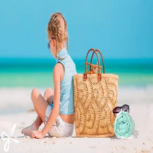 Beach scene lifestyle detail featuring soft cotton beach towel and straw bag on sand.
