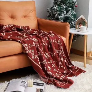 Cozy red knit throw blanket with festive Christmas patterns draped over a modern sofa.