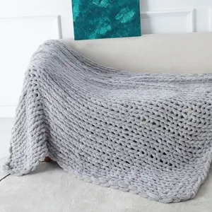 Detailed shot of grey chunky knit chenille blanket draped on cozy beige sofa home decor scene.