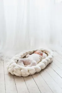Grob gestricktes Baby Nestchen Fotostütze Detail, weicher Wollschlafkorb auf weißem Boden.