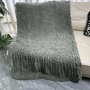 Detailed view of a soft sage green chunky knit chenille blanket draped on a cozy leather sofa.