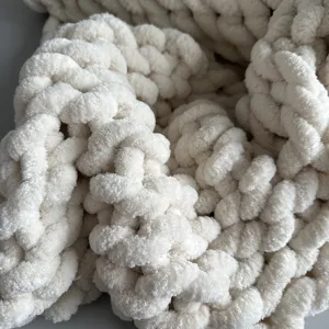 Close-up detail of soft chunky knit chenille blanket texture, fluffy milky white yarn fabric.