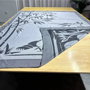 Gewebte Jacquard-Wohndecke mit Panda- und Bambus-Motiv, präsentiert auf einem Holztisch.