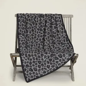 Vista dettagliata di una morbida coperta in maglia leopardata grigia e nera su sedia di legno.