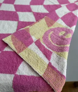 Close-up view of a pink and white checkered plush blanket featuring a cute woven smiley face.