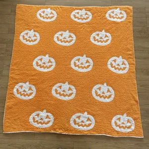 Orange knitted blanket with white jack-o-lantern pattern, soft sofa throw for autumn.