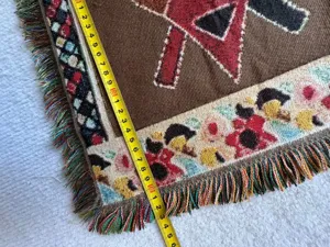 Gewebtes Wandteppich-Detail mit bunten geometrischen Mustern und dekorativen Fransenrändern.