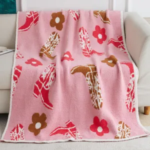Pink knit blanket featuring stylish cowboy boots and cute floral patterns, detail shot.