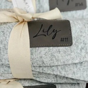 Cozy grey knit blanket with custom leather tag rolled and tied with beige ribbon.