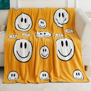 Cozy yellow knitted throw blanket with cute white smiley face pattern, soft fleece fabric.