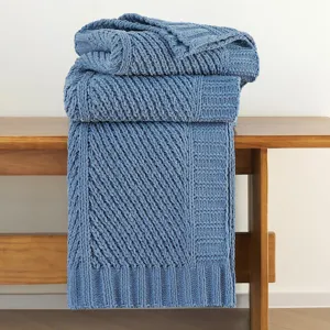 Blue knitted throw blanket detail showing soft textured fabric draped neatly over wooden bench.