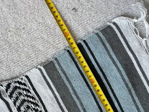 Woven Mexican blanket detail showing geometric stripes and tassels, perfect for beach and picnic.