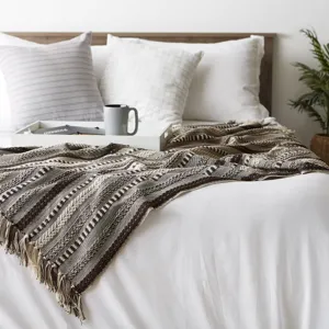 Vue détaillée d'une couverture à franges jacquard tissée aux motifs ethniques sur un lit confortable.