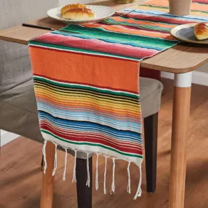 Close-up detail of colorful Mexican striped table runner with white fringe on wooden table.