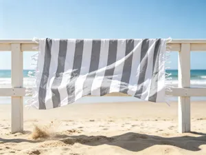 Vista dettagliata di un telo mare a righe grigie e bianche con frange sulla staccionata.