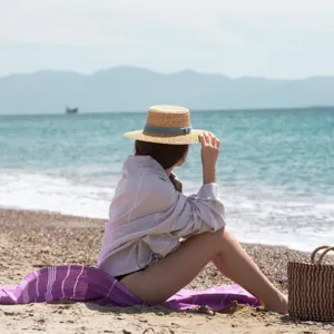 Scenic outdoor beach lifestyle detail view featuring woven striped towel and cozy blanket.
