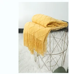 Nahaufnahme einer gemütlichen gelben Kuscheldecke mit Fransen auf einem modernen Drahttisch.