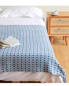 Detailansicht der blau-weißen karierten Strick-Wohndecke mit Fransen im gemütlichen Schlafzimmer.