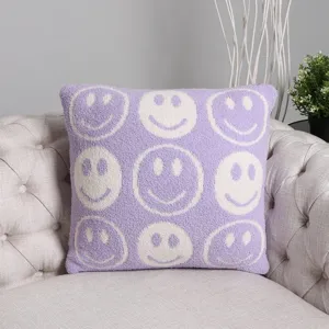Detailed view of soft purple knit throw pillow featuring a cute white smiley face pattern on sofa.