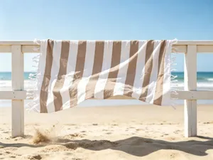Primo piano di un telo mare a righe marroni e bianche con frange su una staccionata di legno.