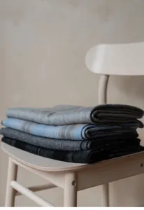 Folded cozy wool blankets detail view on wooden chair, warm home decor lifestyle texture shot.