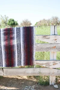 Outdoor blanket detail view showing striped geometric pattern and texture draped on a rustic fence.